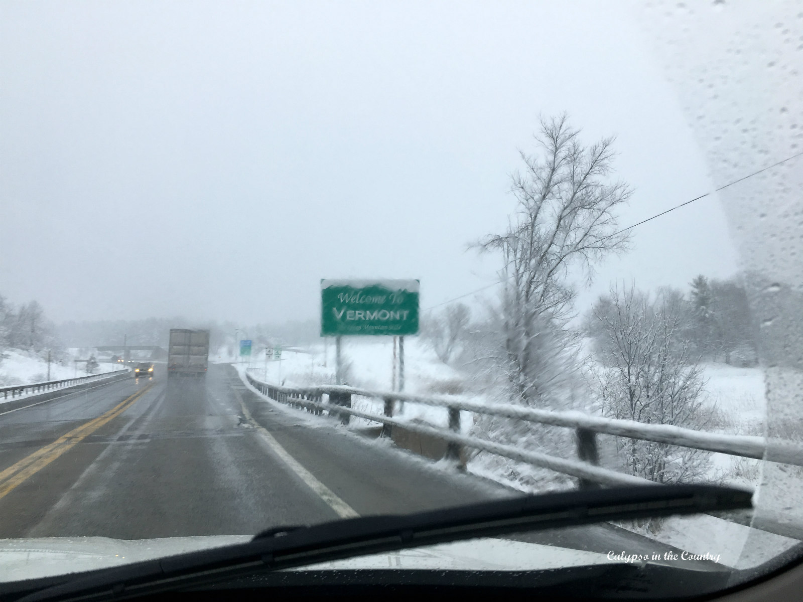 Snowy wet road and green Welcome to Vermont sign