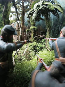 Diorama of 19th-century soldiers with muskets in the bush, aiming at a Maori by a pa fence.