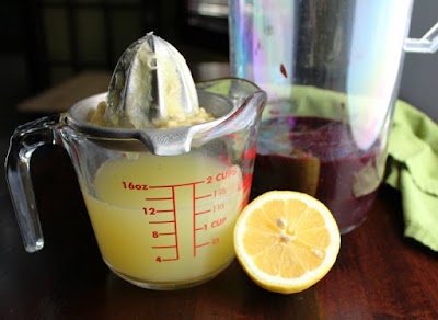measuring cup with juicer and lemon half and pitcher with fresh blackberry puree in it