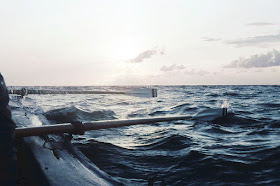 Blick aus einem Ruderboot auf die Ostsee. Die Ruder sind zu erkennen, leichte Wellenbewegung über den Wasser, die Sonne am Horizont.