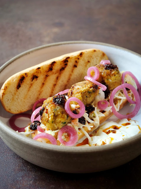 Falafel-Sandwich mit Coleslaw, süßsauren Zwiebeln, Joghurt-Sauce und Chiliöl