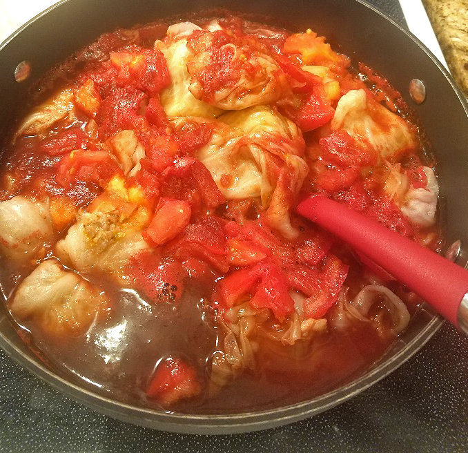 this is a pot of stuffed cabbage rolls in a rich tomato sauce simmering on the top of the stop. It has rice and meat inside of the rolled up soft cabbage.