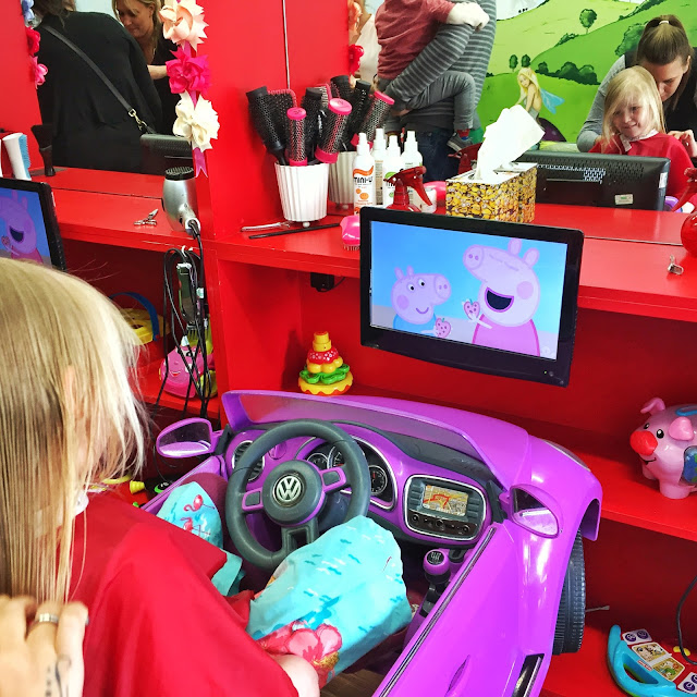 4 year old girl sitting in a car getting her haircut and watching Peppa Pig