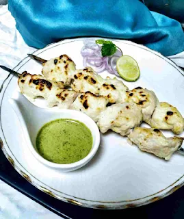 Chicken malai kebab Shewer on a plate with green chutney and onion slices