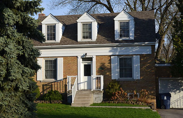 a colonial-looking house with three gabled windows on the second floor, and a green front lawn