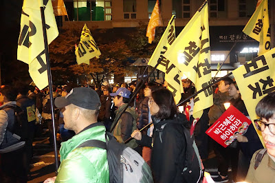 Gangjeong-vilaĝanoj de Jeju Island portas siajn apartajn "Neniu Mararmean Bazon" flagojn dum protesto en Seulo, Sud-Koreio la 12-an de novembro postulante la eksiĝo de dekstrula prezidanto Park Geun-Hye. Ĝis unu miliono da koreoj marŝis al la kunmetaĵo de la prezidanto (Blua Domo)