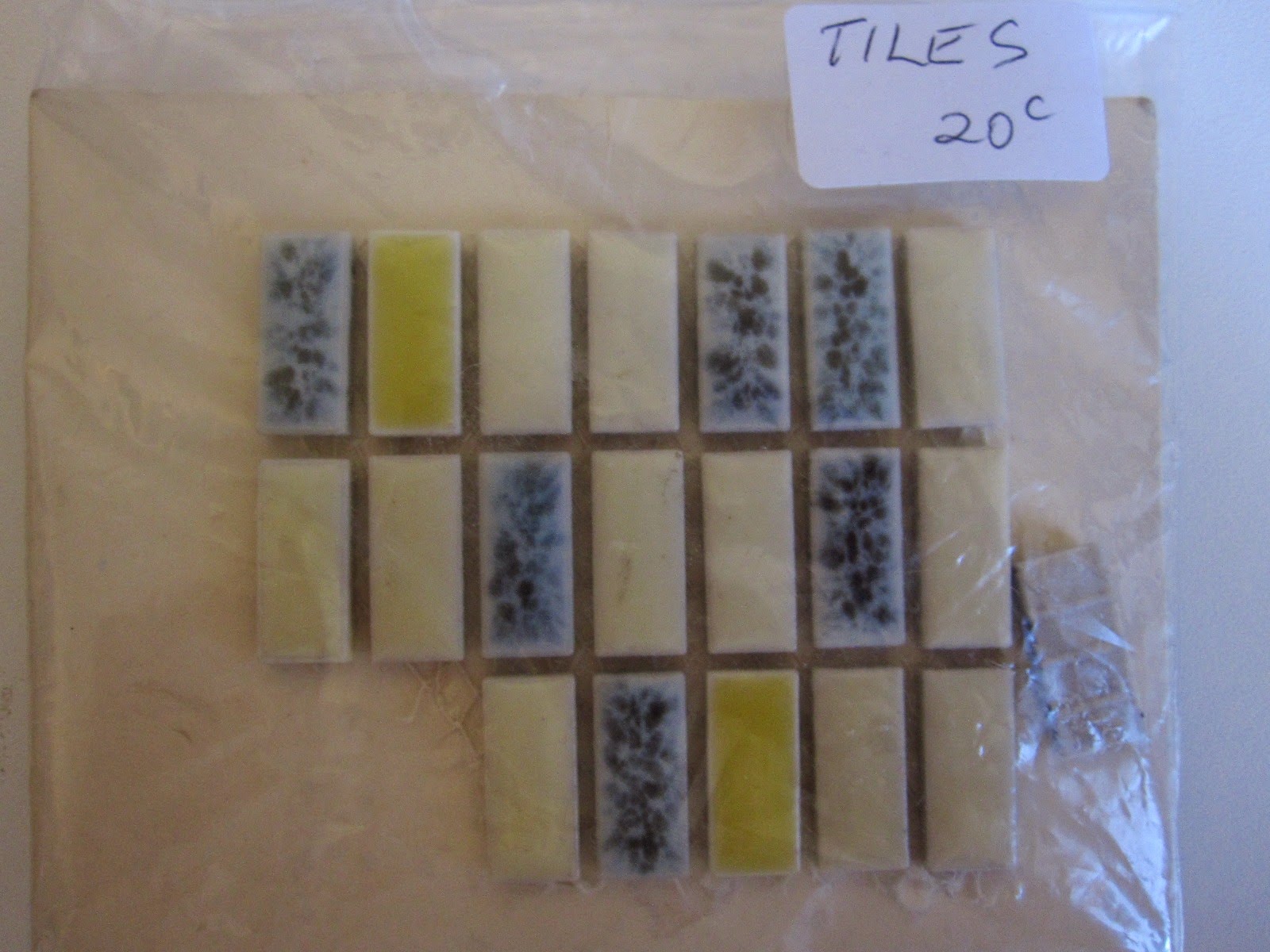 Bag, marked 'tiles 20c', containing 20 vintage dolls house miniature tiles in shades of cream, grey and yellow.