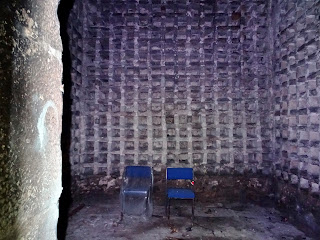 Photo of the interior of the Doocot with over one thousand five hundred stone nesting boxes inside for pigeons.  Two blue chairs sit inside the doocot facing out towards the entrance door.  Photo by Kevin Nosferatu for the Skulferatu Project.