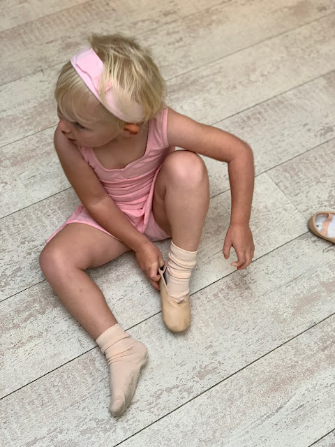 A 3 year old putting on ballet shoes for dance class