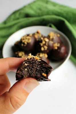 You are just three ingredients away from the most fabulous chocolate dipped peanut butter chocolate cookie truffles. These candies are easy to make and super delicious! hand holding peanut butter chocolate cookie truffle with bite missing, bowl of remaining oreo balls in background
