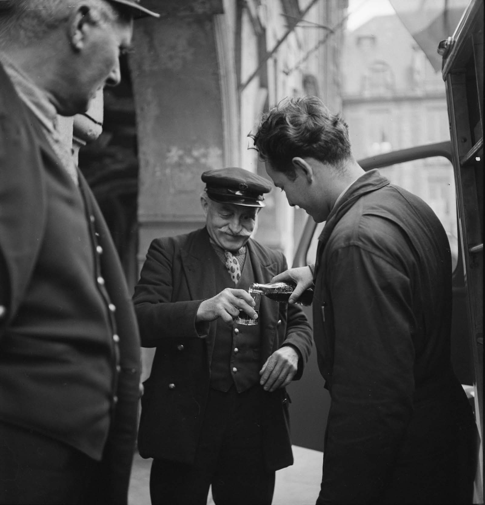 Egy járókelő azt figyeli, hogy egy ember egy üveg Coca-Cola-t egy pohárba önti egy mosolygó, idős ember, Párizsban, Franciaországban.