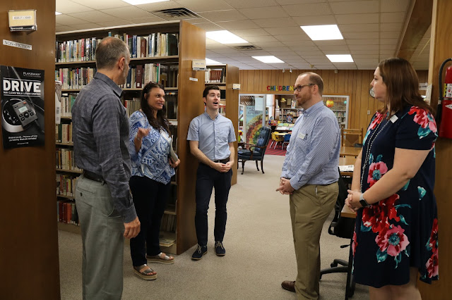 Two women and three women stand in a semi-circle in a library talking together.