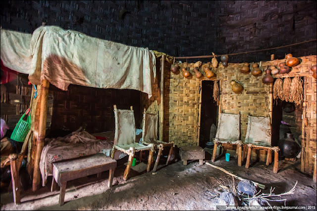 Внутреннее убранство дома. Пол глиняный, на бамбуковых перегородках висит домашняя утварь, стоят стулья из бамбука и коровьих шкур, кровать.