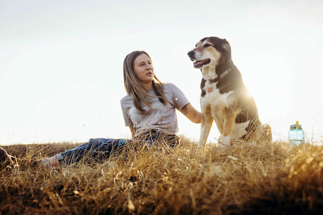 Writer Trina Moyles sits on the dried grass with her dog, Holly. The Writer's Pet and Lookout