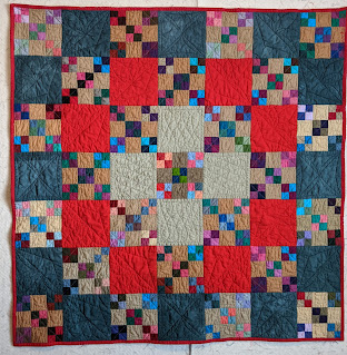 Small nine-patch blocks alternate with cadet blue, bright red, and tan solid fabric blocks and highlight a variety of free motion quilting.