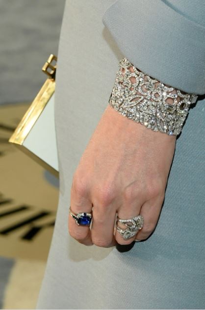 Il dettaglio di bracciali ed anelli in oro bianco, diamanti e zaffiro indossati da Charlize Theron al braccio sinistro.
