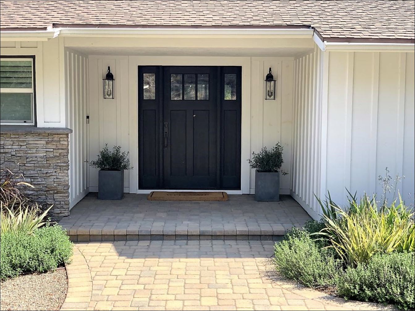 mid-century ranch house exterior home remodel and improvements drought-tolerant plants landscape pavers stone pea gravel black craftsman entry door privacy gate board and batten black and white