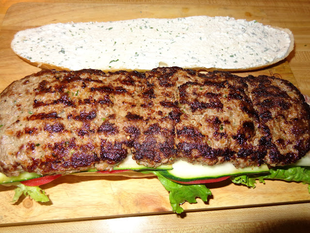 Kofta, es una preparación hecha con carne molida, muy popular en el medio oriente, la India, Egipto, Turquía y los Balcanes. Se usa mucho en pinchos asados (kebab)  a la parrilla, se sirve con tomates, pepinos, lechuga, aderezo de yogur y pan pita. KOFTA SANDWICH PORCIONES: 8 INGREDIENTES PARA ALIÑAR LA CARNE 1.077 g. / 38 oz. de carne molida 2 panes largos de 36 cm. / 14ʺ pulgadas de largo aproximadamente ¾ taza de cebolla picada bien finito 2½ cucharadas de perejil finamente picado 3 dientes de ajo picados bien fino 2 cucharaditas de comino en polvo ½ cucharadita de coriandro en polvo. (Semillas de cilantro en polvo) 1 cucharadita de sal 1/ 4 cucharadita de ají seco triturado  PREPARACION En un recipiente redondo, mezclar bien todos las especias con la carne. Dividir la carne en 2 partes. Sobre una hoja de papel cera untar un poquito de aceite y estirar una parte de la carne de manera que tenga el mismo ancho y algo más largo que le pan. Digo, algo más largo porque la carne se encogerá al cocinar. Poner en el refrigerador hasta el momento de uso.  Calentar bien una plancha y asar la carne por ambos lados, ayudándose con 2 espátulas para dar vuelta la carne. VEGETALES PARA EL SANDWICH Hojas de lechuga 3 tomates cortados en rodajas 1 pepino con la piel, cortado en rodajas bien delgadas 1 cebolla roja, cortada en pluma y sazonada con 2 cucharadas de aceite de oliva, 1 cucharada de vinagre de vino, sal, pimienta y 1 cucharada de cilantro picado. ADEREZO DE YOGUR ½ taza de yogur espeso como el griego 1 cucharada de jugo de limón 1 diente de ajo picado bien fino ½ cucharada de perejil picado ¼ cucharadita de sal 1/8 cucharadita de pimienta en polvo MONTADO DEL SANDWICH Cortar el pan a lo largo y aplicar el aderezo en ambos lados interiores del pan. En la parte inferior del pan, poner capas de lechuga, tomate, pepino, carne asada y cebolla en vinagreta. Cerrar el pan, dividir con palillos de sándwiches y cortar en 4 porciones cada sándwich