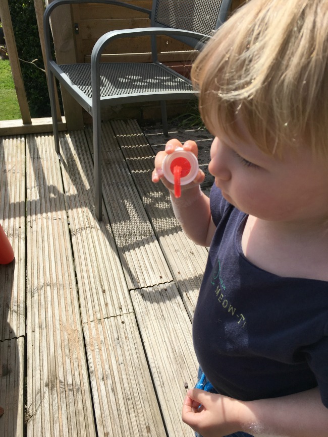 toddler with bubble wand blowing bubbles