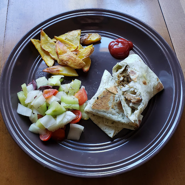 Falafel wrap with vegan sausage and onions, greek salad, and homemade fries on a plate