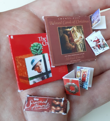 Hand holding a selection of one twelfth scale Christmas cards, Christmas record covers and box of Scorched Almonds.