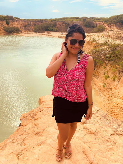 Passeio Quadriciclo em Parnaíba mulher morena, jovem, cabelo preto, oculos escuros, blusa rosa e saia preta com a paisagem de uma lagoa verde ao fundo
