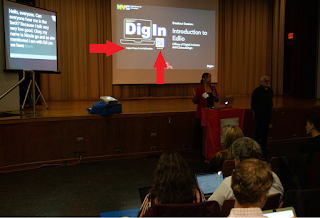 Woman speaking at podium to an audience in an auditorium. There is a screen behind her featuring a slide that provides the session title as well as how to access content. 