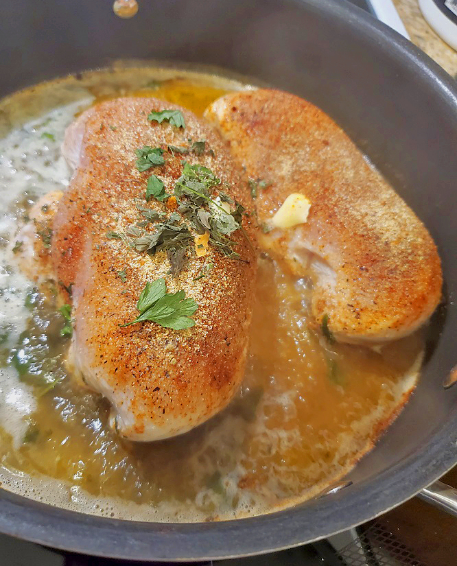 these are boneless seasoned chicken breasts in butter frying in a pan