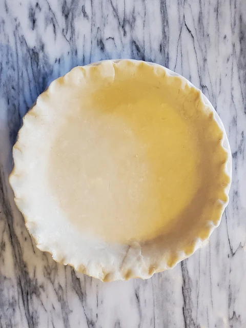 overhead of empty pie crust on marble countertop