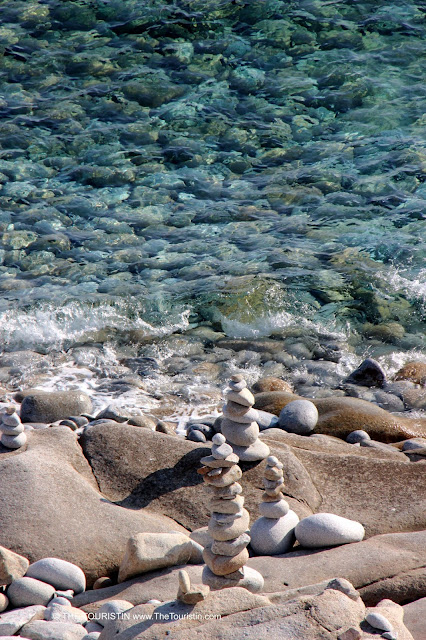 Round large pebbles next to the clear green-blue coloured sea.
