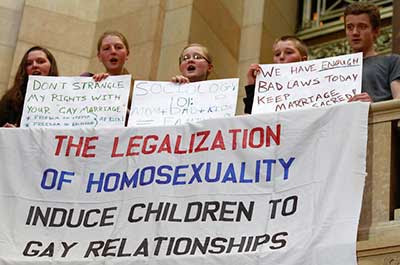 Neatly handmade banner hanging from a Capitol railing reads THE LEGALIZATION OF HOMOSEXUALITY INDUCE CHILDREN TO GAY RELATIONSHIPS