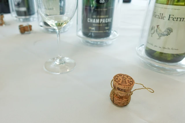 A champagne cork, a glass and wine bottles in the background