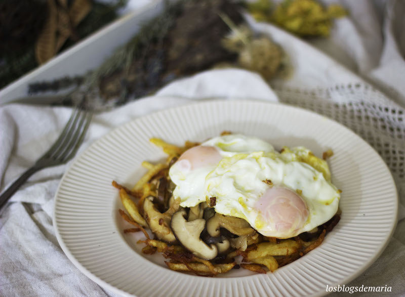 Huevos fritos sobre champiñones salteados y patatas pajas fritas