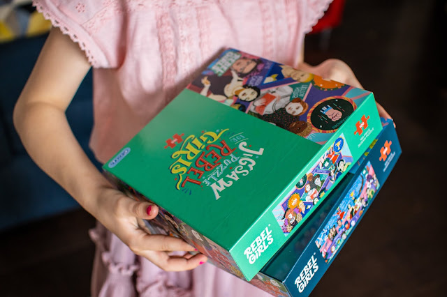 A close up of a young girl holding 2 Rebel Girls jigsaw puzzle boxes