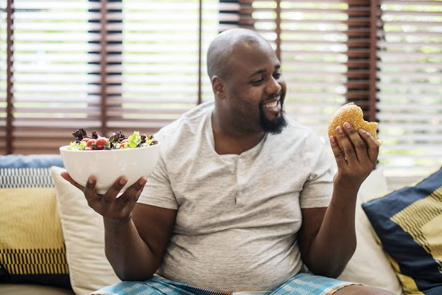 Hombre con sobrepeso decidiendo entre una hamburguesa o una ensalada