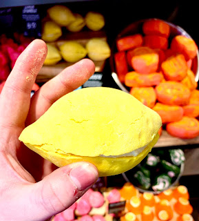 A light white pale hand holding a bright yellow glittery lemon shaped bubble bar filled with pale yellow butter in the middle on a bright background