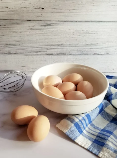 bowl of eggs, whisk and blue plaid tea towel