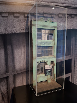 1/24 scale model facade of an old three-storey commercial building on display in an art gallery.