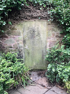 A gravestone forms part of one of the walls within the tomb.  Ivy grows around it and on the stone can be seen a grinning skull and crossbones and an inscription. Photo by Kevin Nosferatu for the Skulferatu Project.