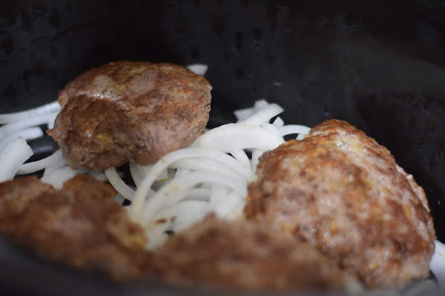 The steak patties on top of the onions in the slow cooker. 