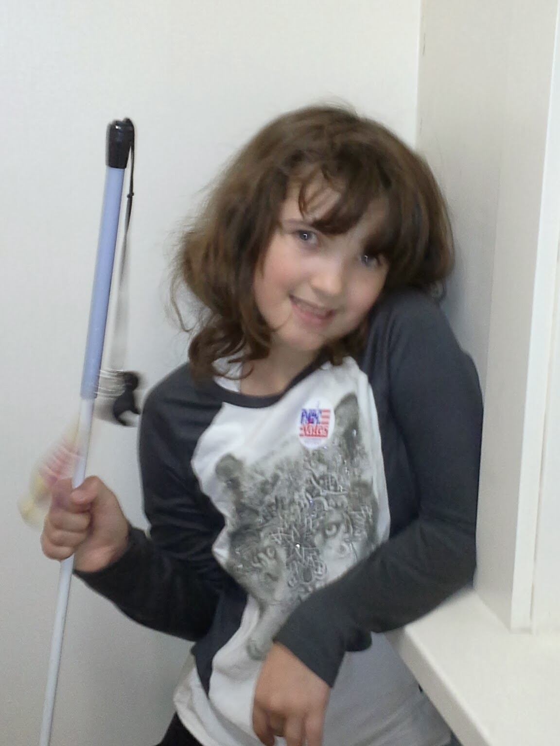 A girl with dark hair wearing a wolf long sleeve shirt and holding a white cane smiles