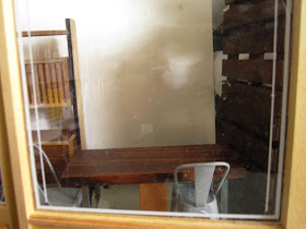 View through a mock up of the front of a modern dolls' house miniature cafe showing a pallet wall and a table and cafe chairs.