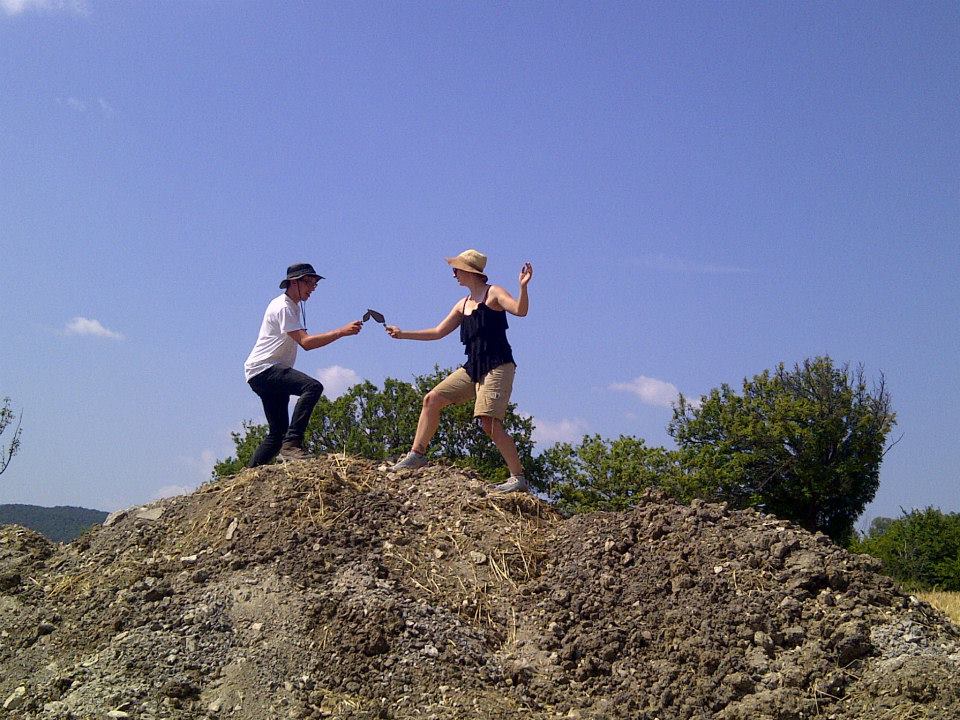 Two meople on top of a dirt mound have a mock swordfight.