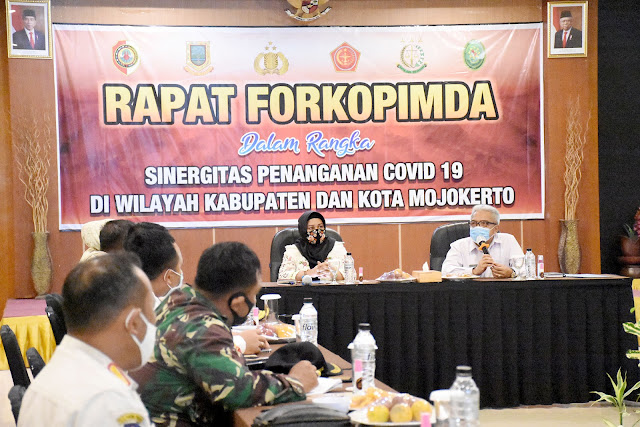 Pemkab Mojokerto dan Pemkot Mojokerto Bersatu Lawan Pandemi Mojokerto - Pjs Bupati Mojokerto Himawan Estu Bagijo, menyebut sebaran pandemi Covid-19 tidak mengenal batas-batas yurisdiksi (wilayah/daerah tempat berlakunya sebuah undang-undang berdasarkan hukum). Khususnya pada wilayah Kabupaten dan Kota Mojokerto yang saling bertumpu satu sama lain. Untuk itu, Himawan mengajak dua pemerintahan ini untuk bekerjasama dan bersinergi dalam menanggulangi pandemi. Hal tersebut disampaikannya Pjs pada rapat gabungan Pemkab/Pemkot Mojokerto, dengan dihadiri Walikota Mojokerto Ika Puspitasari, beserta Forkopimda dan OPD. “Kota Mojokerto ada di tengah-tengah wilayah kami. Saya ingin, kondisi ini tidak menjadi barrier kita dalam menangulangi pandemi. Wabah tidak kenal batas yurisdiksi. Warga kami yang kerja di kota juga ada, dan sebaliknya. Maksud saya, dari pertemuan ini kita bisa menyatukan sinergi,” kata Pjs Bupati Mojokerto, Selasa (7/10) siang di Hotel Ayana Trawas. Sepakat dengan Pjs Bupati Mojokerto, Walikota Mojokerto Ika Puspitasari juga menyatakan kesepahamannya terkait penanganan Covid-19 yang tidak mengenal batasan. Ning Ita ingin agar sinergi penanganan dapat dimulai dari penegakan sanksi, penanganan dan perawatan pasien, penyelenggaraan pendidikan hingga upaya-upaya pencegahan klaster. “Saya sepakat, wilayah kita tidak bisa dipisahkan. Kebijakan masing-masing pemerintahan juga kadang tidak bisa dibedakan masyarakat. Mana kabupaten, mana kota. Begitupun juga dengan sanksi yang terkadang ada sedikit perbedaan,” kata Ning Ita. Secara rinci, Ning Ita juga menjelaskan jika dari 6 RS kota, yang dilayani juga ada yang berasal dari warga kabupaten. Masalah juga timbul, terkait keterbatasan lahan pemakaman korban Covid-19 yang kerap menimbulkan gejolak status kewilayahan. “Jumlah warga kota sekitar 140 ribu. Jumlah itu sebetulnya bisa terlayani di dua sampai tiga RS yang ada. Sebenarnya tidak ada persoalan, hanya perlu koordinasi. Di kota, lahan pemakanan covid sangat terbatas. Ditambah persepsi masyarakat, kerap menolak jenazah jika bukan warga asli,” tambah Ning Ita. Beberapa problem juga dikupas oleh Ning Ita dalam pembahasan ini. Antara lain pendidikan sekolah, munculnya klaster ponpes dan perkantoran termasuk lapas. “Di kota ada sekitar 33 perkantoran termasuk perbankan. Seluruh aktivitasnya melayani masyarakat daerah manapun. Ini perlu kita buat strategi bagaimana ada standarisasi yang sama, antara kabupaten maupun kota. Itu bisa jadi klaster, lalu nular ke keluarga, termasuk klaster lapas. Kami sudah rapid. Tapi tetap butuh sinergi bersama,” tandas Ning Ita. Menanggapi hal di atas, Pjs Bupati Mojokerto menjabarkan beberapa hal penting soal regulasi, operasi, penerapan sanksi. Sistem treatment dari semua tindakan penanganan Covid-19, diminta agar punya standard yang sama. Pjs Bupati juga menghendaki adanya informasi tunggal demi terwujudnya sinergi. “Saat penerapan di lapangan, mungkin kita ada sedikit perbedaan. Namun, basis regulasi sebenarnya sama. Begitu juga dengan penentuan reward-punishment yang tepat saat penegakan sanksi protokol kesehatan. Perlu ada single information between us, supaya kita ini sinergis,” kata Pjs bupati. Pjs Bupati Mojokerto pun memastikan jika izin membuka sekolah luring, telah mendapat restu Gubernur Khofifah Indar Parawansa. Meski dengan beberapa catatan, hal tersebut dapat menjadi motivasi dalam menekan Covid-19. “Untuk pendidikan, kita sudah diizinkan Ibu Gubernur. Tentu dengan aturan yang ketat. Kita harus hijau dulu, yang masuk sekolah pun bertahap 25 persen secara bergantian. Izin rekomendasi juga harus dikantongi. Kita keluar dari forum ini, harus dengan action plan. Saya akan tugaskan asisten 1, 2 dan 3 dibantu semuanya,” tambah Pjs Bupati. Kapolresta Mojokerto AKBP Deddy Supriyadi, dalam pertemuan ini turut menjawab adanya keluhan perbedaan sanksi denda pelanggar protokol kesehatan. Tidak hanya di pusat keramaian masyarakat, Kapolres juga menyarankan adanya operasi yustisi skala mikro secara rutin. Kapolresta juga mengusulkan adanya reward bagi desa yang hingga sekarang dapat bertahan sebagai zona hijau (zero case), misalnya seperti beberapa desa di Kecamatan Dawarblandong. “Perbedaan itu sebenernya karena masa transisi, komitmennya tetap sama yakni protokol kesehatan harus tegak. Senjata kita yang utama yustisi. Berdasarkan penelitian UNAIR, yustisi punya andil dalam menurunkan status dari merah ke oranye seperti yang terjadi di Jawa Timur terkini. Yustisi kalau bisa harus sampai tingkat desa, kelurahan bahkan dusun. Reward bagi yang patuh, dan masih hijau sampai sekarang juga harus ada,” kata Kapolresta. Sementara itu, Kapolres Mojokerto AKBP Dony Alexander, pada paparannya mengutarakan problem pengendalian angka kematian akibat Covid-19 yang belum bisa ditekan. Dony melihat hal tersebut kemungkinan bisa disebabkan perbedaan treatment antara RSUD dan RS swasta. “Belakangan memang jumlah terinfeksi mulai turun. Namun jumlah kematian Covid-19 ternyata belum bisa ditekan. Ada benang merah yang belum bisa diurai. Bagaimana pengendalian angka kematian Covid-19 ini. Mungkin saja ada perbedaan treatment antara RSUD dan RS swasta dalam menangani pasien Covid-19. Kita harus menyatukan visi dan misi, merumuskan standarisasi treatment terbaik bagi pasien,” papar Dony. Dony pun menambahkan, bisa jadi tingginya kematian Covid-19 karena pasien yang memang memiliki komorbid atau penyakit penyerta. Untuk itu, Ia menyarankan pengadaan bank data medical check up masyarakat. “Tiap kecamatan wajib punya medical check up masyrakatnya. Dari situ bisa ditelusuri mana sekiranya yang komorbid agar dapat dilakukan penanganan lebuh cepat dan tepat,” tandas Dony. (Jayak)