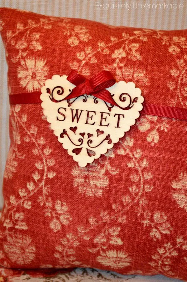 Red pillow with wooden heart that says SWEET attached with ribbon