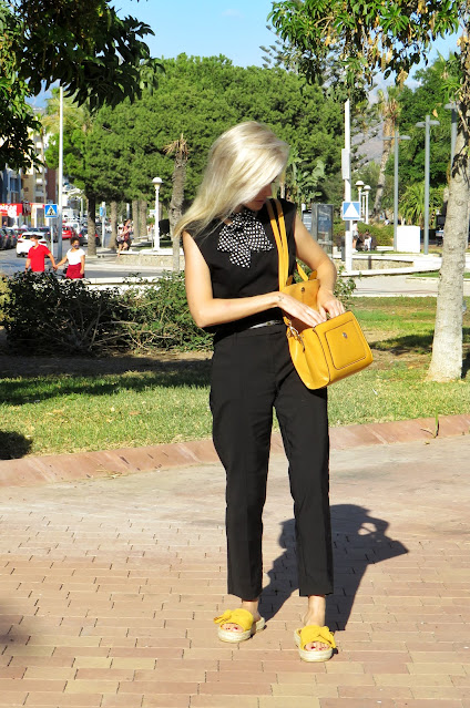 Alejandra Colomera con camiseta negra, pantalón formal negro, lazo en el cuello negro con lunares blancos y complementos mostaza