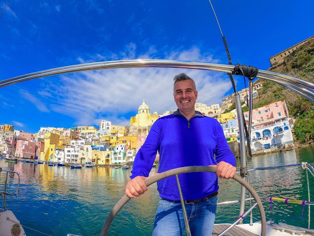 Gennaro de Concilio is driving a sailboat in the background colorful houses of the raccoon fishermen