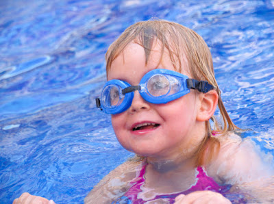 Picture of a happy child  in the swimming holding onto the edge. This article is about how to prepare your child for swim lessons
