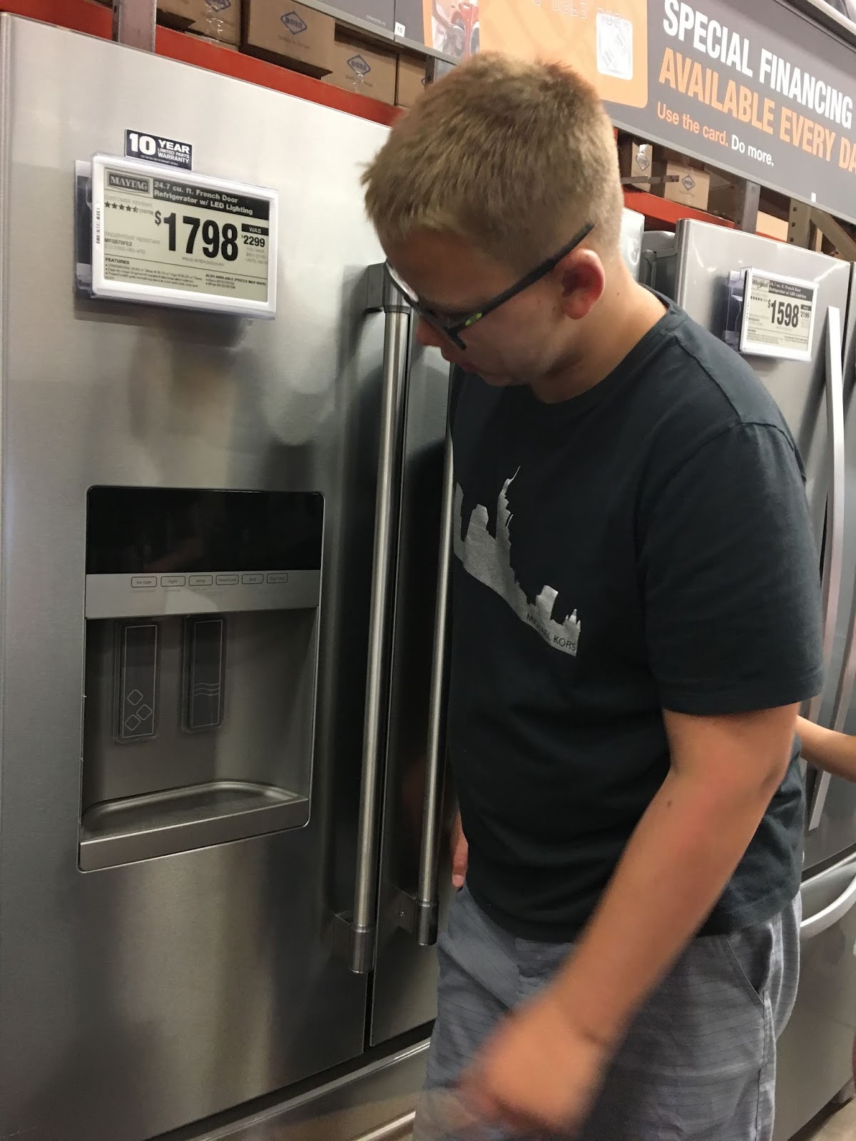 A male teenager examines a refridgerator at the home depot. 