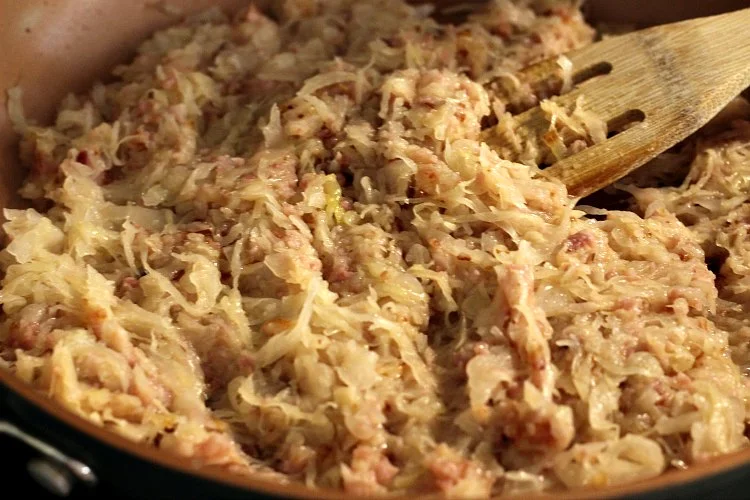 Skillet with wooden spatula showing remaining ingredients added